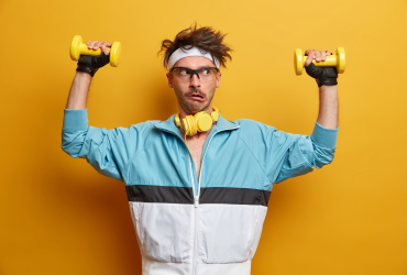 Jovem treina músculos das mãos com halteres, faz todos os esforços para levantar peso, faz reabilitação física, faz exercícios para os braços, posa em casa ginásio, vestido com roupas esportivas.