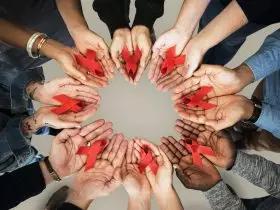 Um grupo de pessoas de várias etnias, mostrando o símbolo do combate ao HIV/AIDS