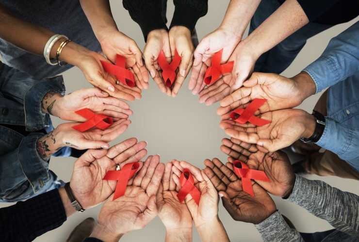 Um grupo de pessoas de várias etnias, mostrando o símbolo do combate ao HIV/AIDS