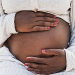 Mulher negra grávida segurando a barriga