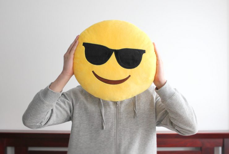 Rosto de emoji sorridente amarelo brilhante usando almofada de óculos escuros sustentada por uma pessoa Por iheartcreative