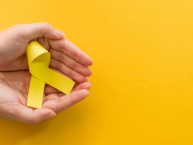 Foto de cima de uma mão feminina segurando uma fita amarela sobre fundo amarelo Por wirestock