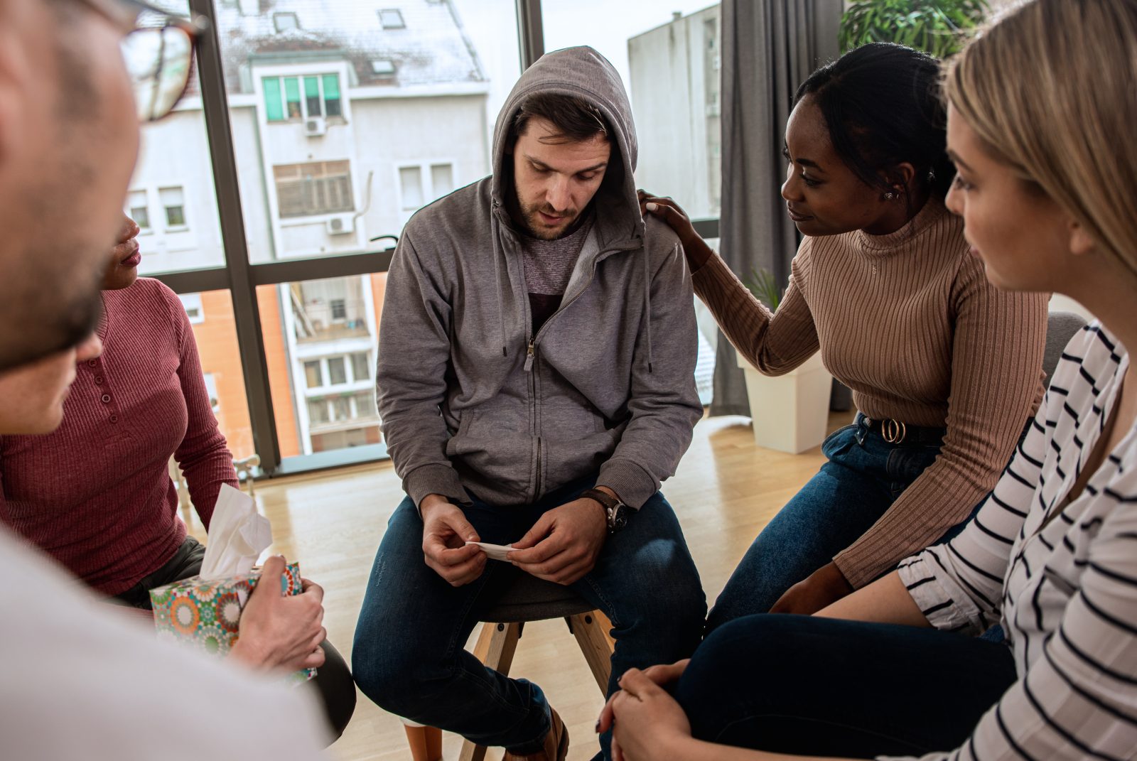 Grupo diversificado de pessoas sentadas em círculo na sessão de terapia em grupo. Por zoranzeremski