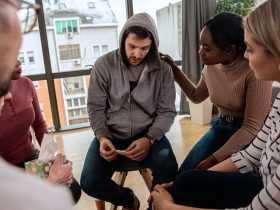 Grupo diversificado de pessoas sentadas em círculo na sessão de terapia em grupo. Por zoranzeremski