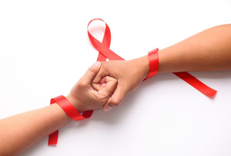 Duas pessoas de mãos dadas com o símbolo de combate ao HIV/AIDS