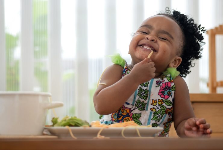 Um criança muito fofa comendo macarrão e alface