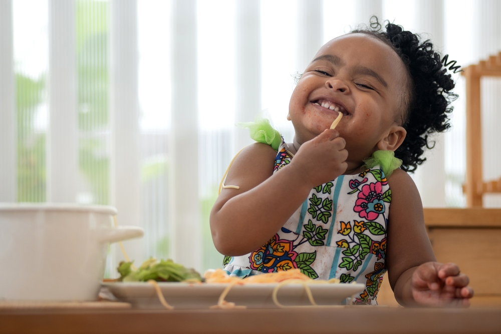 Um criança muito fofa comendo macarrão e alface