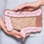 vista parcial da mulher segurando papel feito intestino grosso em fundo cinza Por LightFieldStudios