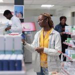 Mulher afro-americana comprando vitaminas em farmácia, instrução de leitura Por DC_Studio