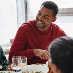 Amigos desfrutando de uma refeição festiva de Natal juntos, compartilhando histórias e risadas em casa Por LightFieldStudios