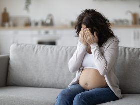 Retrato de uma jovem grávida chorando enquanto está sentada no sofá em casa Por Prostock-studio