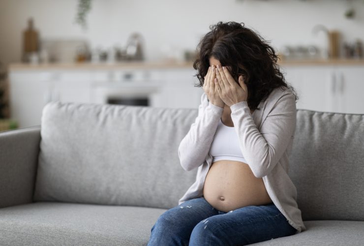 Retrato de uma jovem grávida chorando enquanto está sentada no sofá em casa Por Prostock-studio