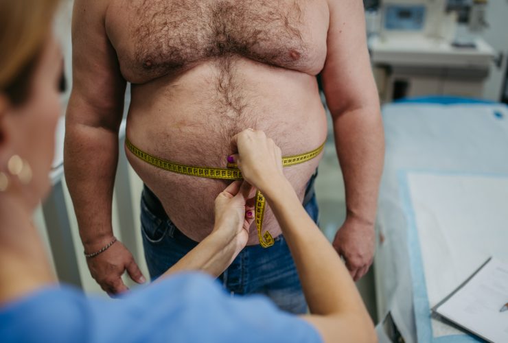 Médica medindo a cintura de um paciente com sobrepeso usando fita métrica. Obesidade afetando o meio Por halfpoint