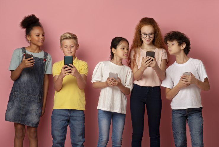 Tecnologias modernas na educação. Crianças multiétnicas usando celulares juntos sobre fundo rosa Por Prostock-studio