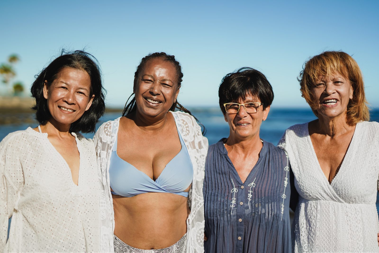 Mulheres multirraciais idosas se abraçando na praia durante as férias de viagem Por SabrinaBracher