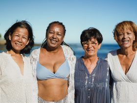 Mulheres multirraciais idosas se abraçando na praia durante as férias de viagem Por SabrinaBracher