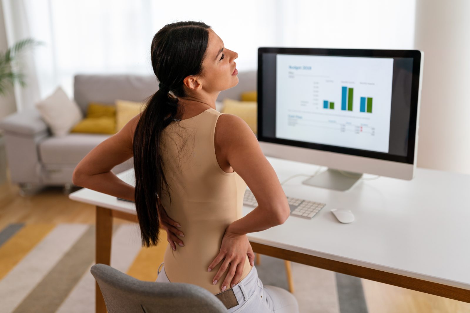 Mulher cansada, trabalhadora sentada à mesa, dor nas costas, dor nas costas forte, conceito de postura incorreta