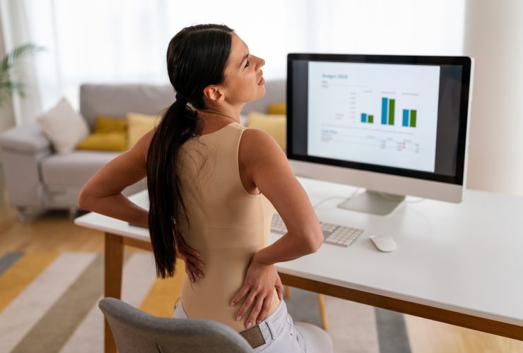 Mulher cansada, trabalhadora sentada à mesa, dor nas costas, dor nas costas forte, conceito de postura incorreta