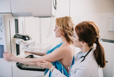 jovem radiologista em pé perto do paciente enquanto fazia o teste de mamografia na máquina de raio-x Por LightFieldStudios