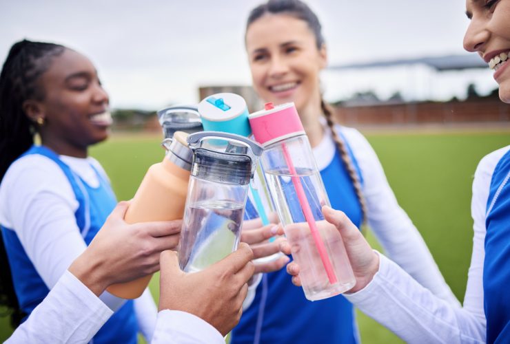 Grupo de mulheres esportivas, grama e garrafa em círculo para brinde, celebração e diversidade com formação de equipe Por YuriArcursPeopleimages