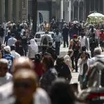 Imagem de pessoas andando em avenida movimentada.