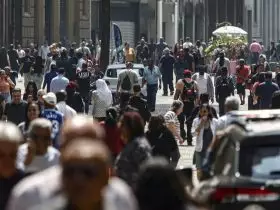 Imagem de pessoas andando em avenida movimentada.