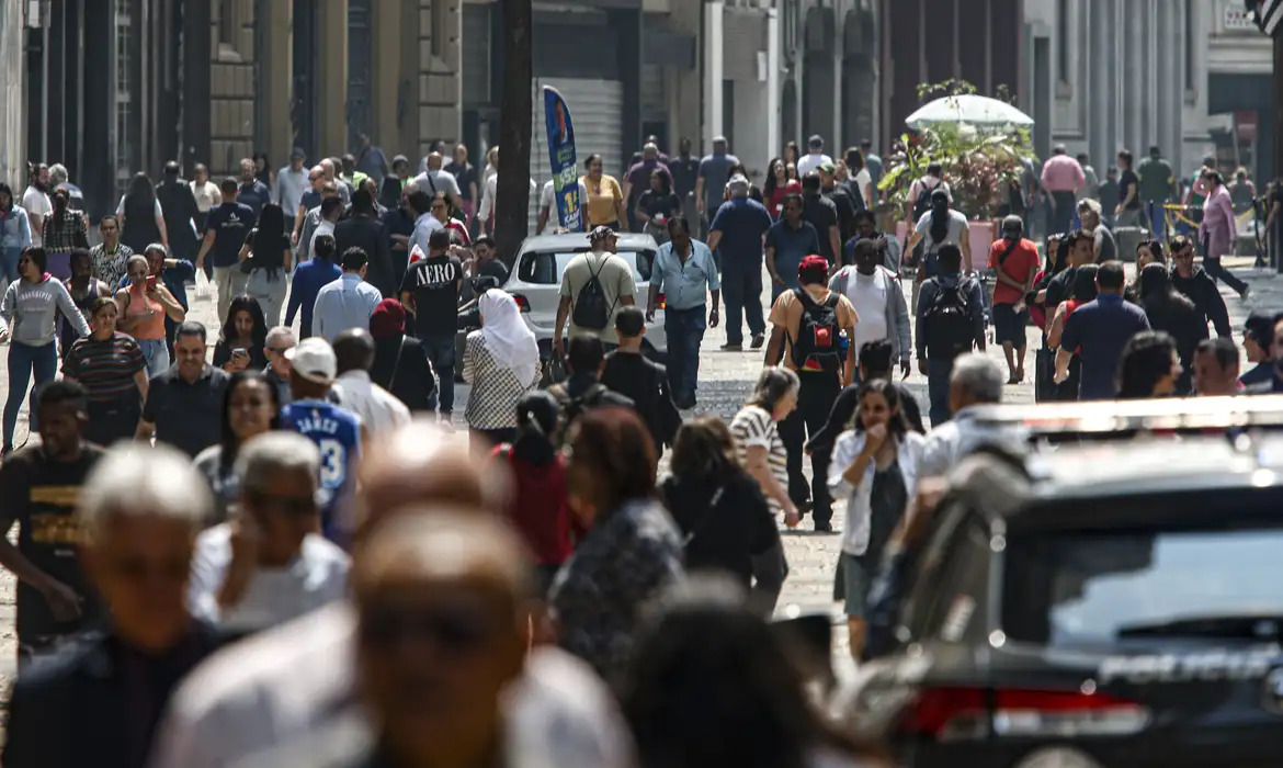 Imagem de pessoas andando em avenida movimentada.