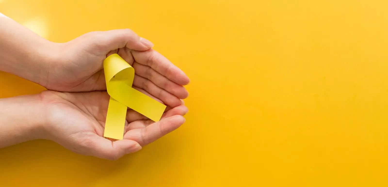 Foto de cima de uma mão feminina segurando uma fita amarela sobre fundo amarelo Por wirestock