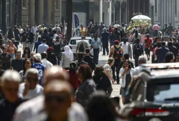 Imagem de pessoas andando em avenida movimentada.
